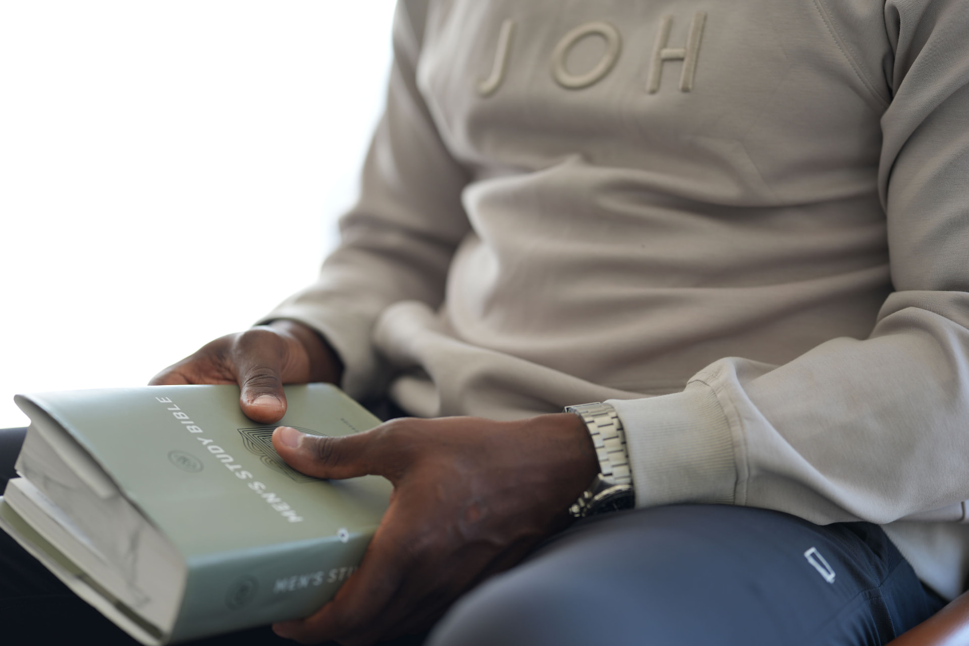 A man in a bone JOH sweatshirt holding a book