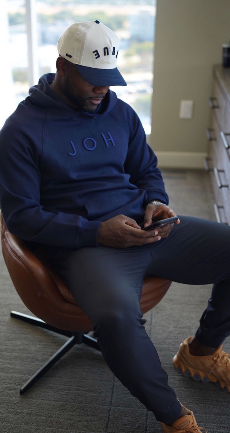 In conversation at work, wearing a navy JOH hoodie, pants, and cap